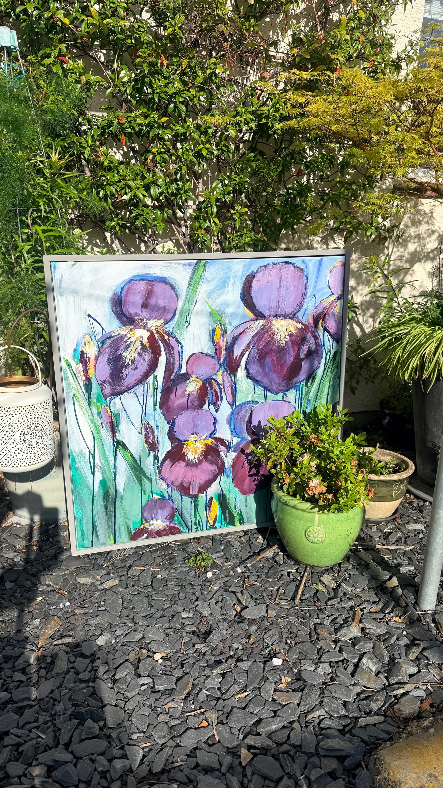 Painting of purple flowers on a gravel surface with plants around